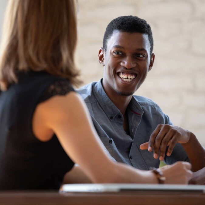 Two work colleagues smiling whilst in conversation at a table