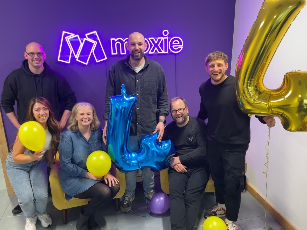 The team stood in front of a neon 'Moxie' sign holding balloons.